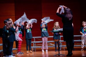 Claire Jurs leads GYC Music Explorers in a song with creative movement featuring which scarves on stage at Tew Recital Hall